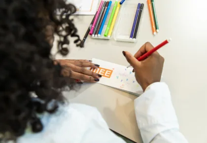 Een jonge meid zit aan een tafel en schrijft creatief haar naam op een papiertje.