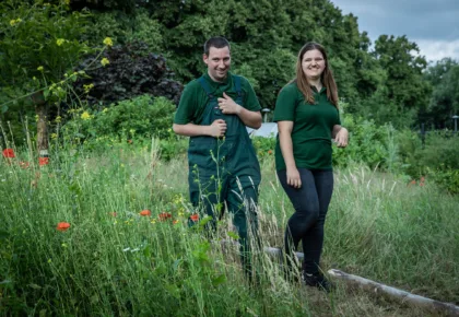 Buiten tussen hoge gras lopen een man en vrouw naast elkaar.